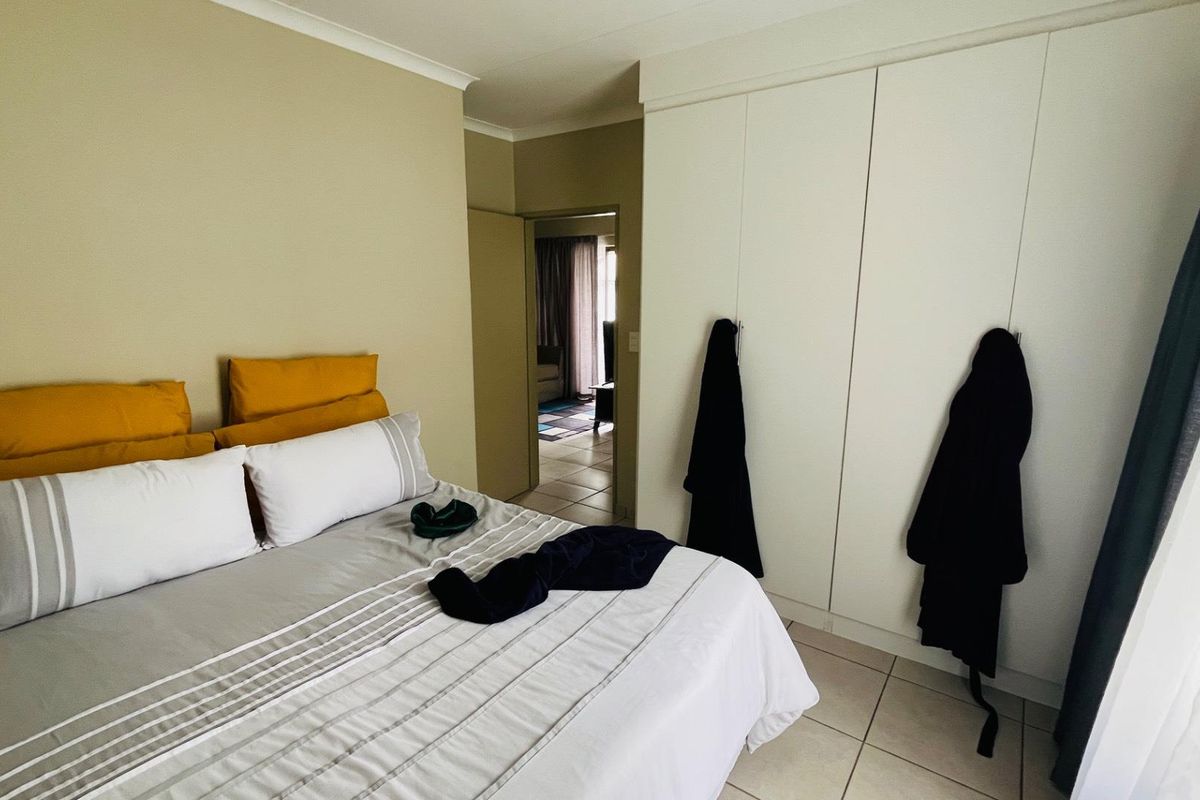 A bedroom featuring built-in floor-to-ceiling wardrobes and tiled flooring, with a doorway leading to an adjacent living area.