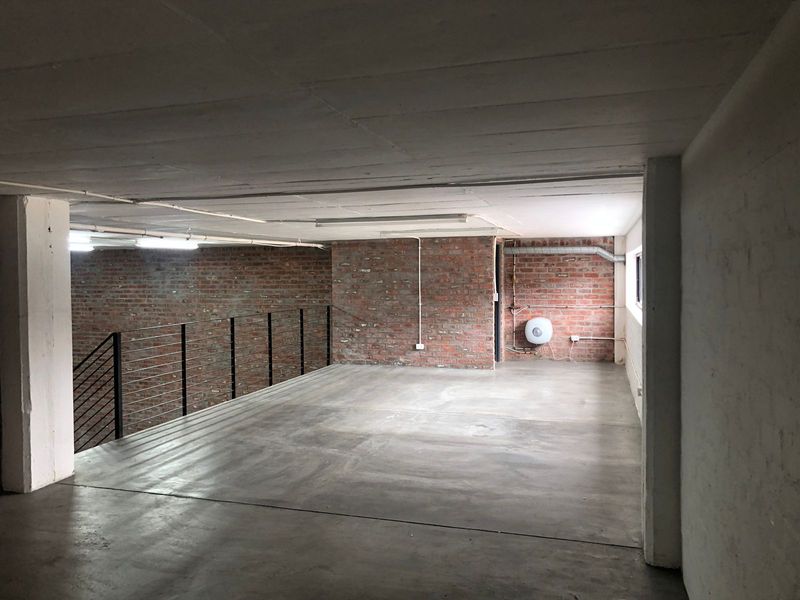 An expansive, industrial-style open plan space featuring exposed brick walls, polished concrete flooring, and a metal balustrade, offering a versatile blank canvas.