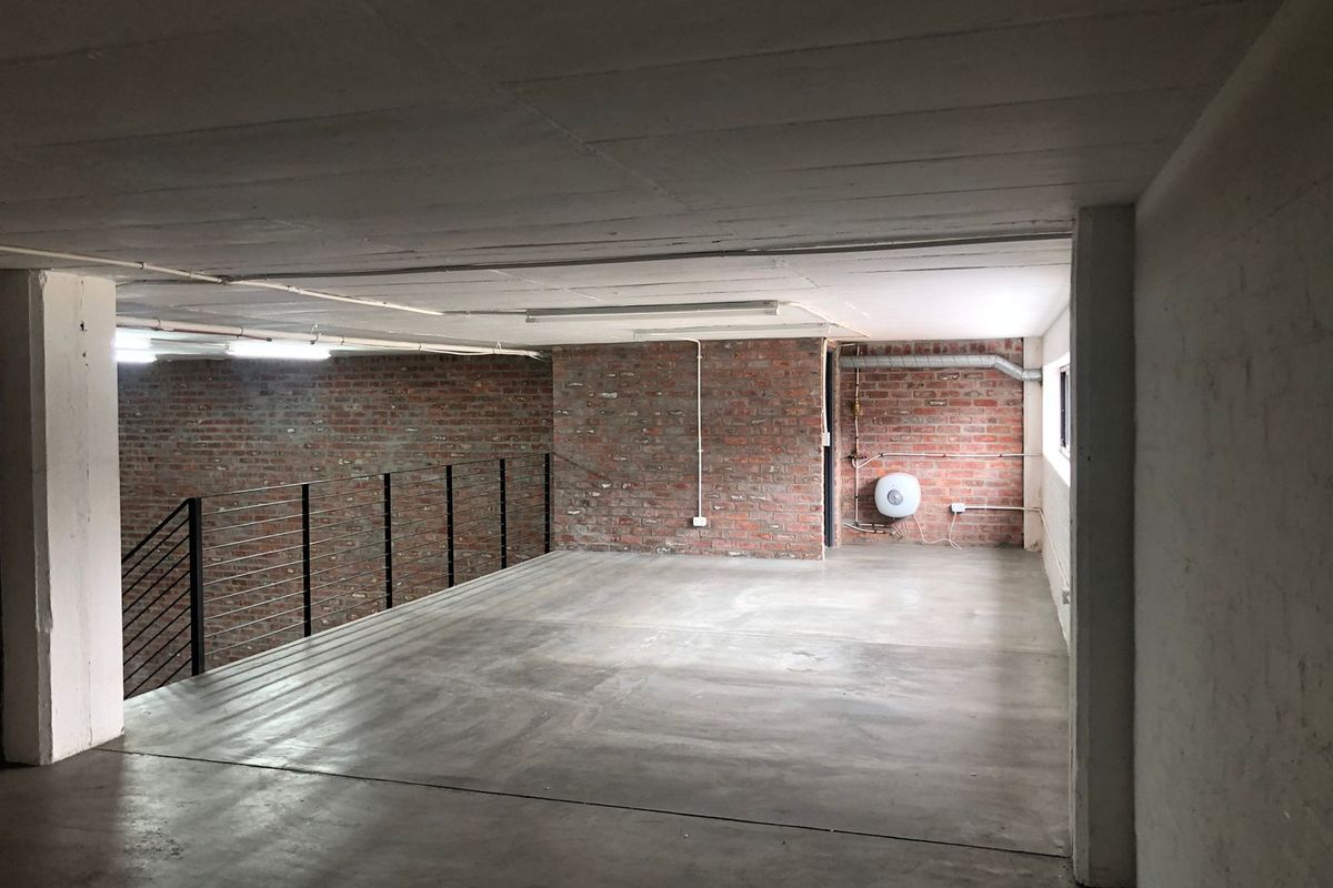 An expansive, industrial-style open plan space featuring exposed brick walls, polished concrete flooring, and a metal balustrade, offering a versatile blank canvas.