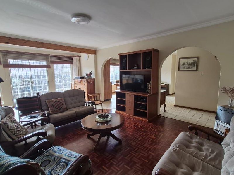 Spacious living room featuring classic parquet flooring, an exposed timber beam, and arched doorways leading to adjacent areas.