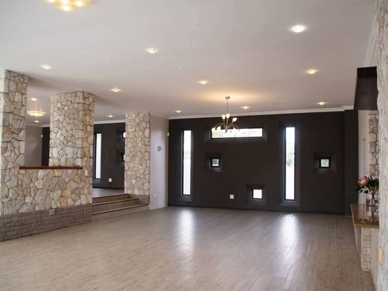 Spacious living area featuring unique stone-clad pillars, modern recessed lighting, and a striking dark feature wall with vertical windows.