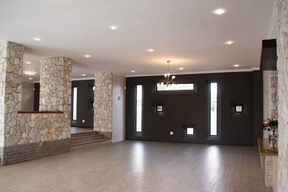 Spacious living area featuring unique stone-clad pillars, modern recessed lighting, and a striking dark feature wall with vertical windows.