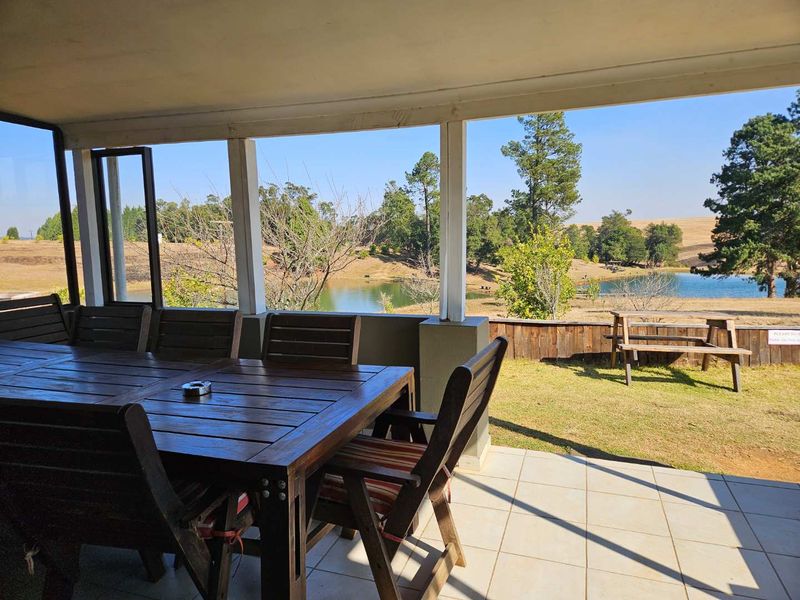 A covered outdoor patio area featuring tiled flooring and timber support posts, overlooking a scenic farm landscape with a dam.