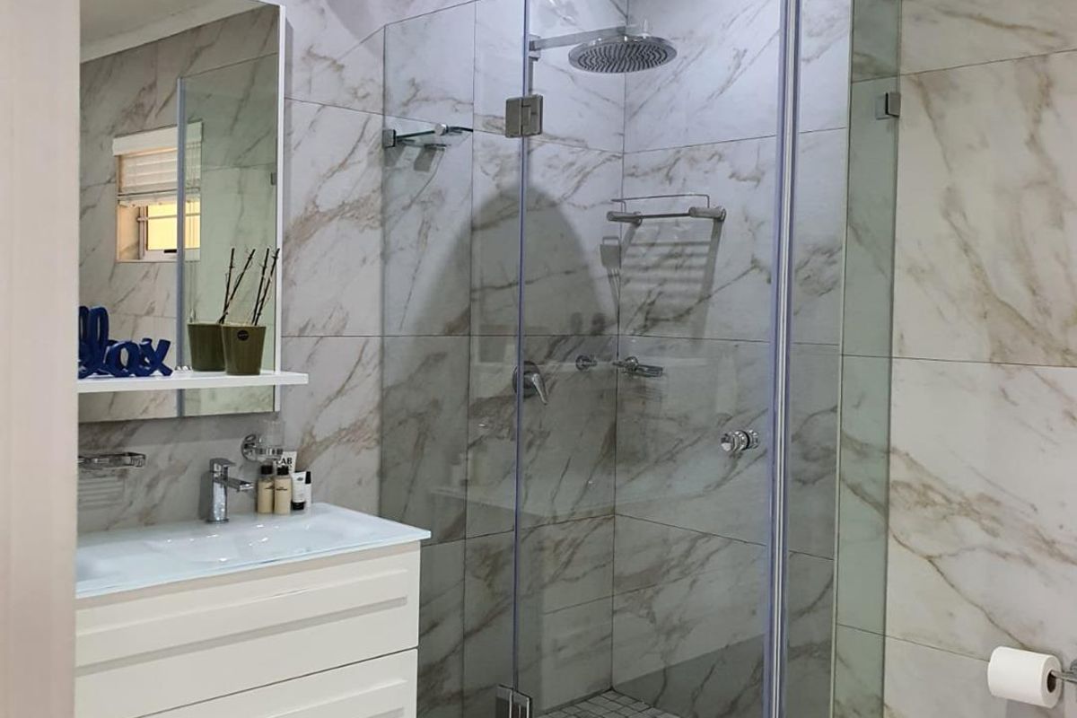 Modern bathroom featuring a glass-enclosed walk-in shower with rainfall showerhead, marble-look wall tiles, and a contemporary wall-mounted vanity with integrated basin.