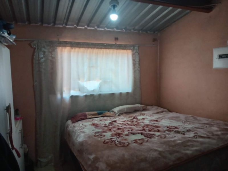 A bedroom featuring an exposed corrugated metal ceiling and basic wall finishes, requiring cosmetic updates to improve the overall aesthetic and comfort.