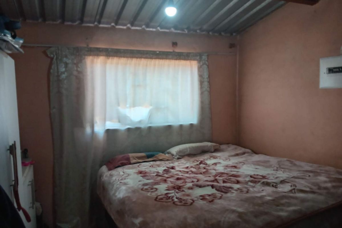 A bedroom featuring an exposed corrugated metal ceiling and basic wall finishes, requiring cosmetic updates to improve the overall aesthetic and comfort.