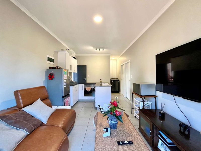 Open-plan living area featuring a compact kitchen with built-in cabinetry, oven, and hob, seamlessly flowing into the lounge space with tiled flooring throughout.