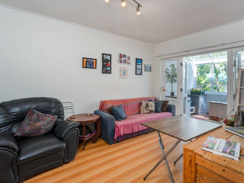A living room featuring laminate flooring, cove cornicing, and track lighting, with direct access through double glass doors to an enclosed patio area.