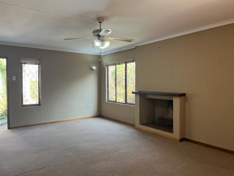 Spacious living room featuring a built-in fireplace, ceiling fan, and large windows with security bars, offering a blank canvas for renovation.