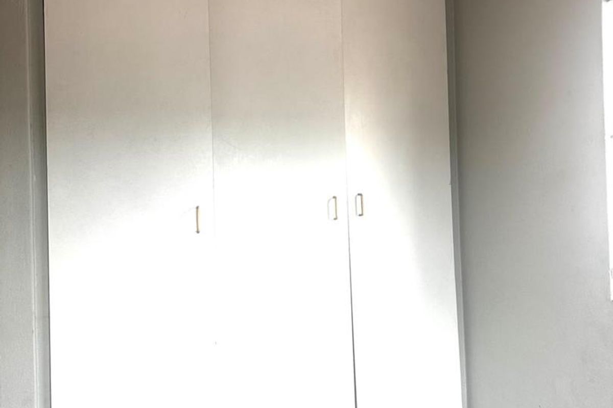 A bedroom featuring built-in white wardrobes with tiled flooring and neutral wall finishes.