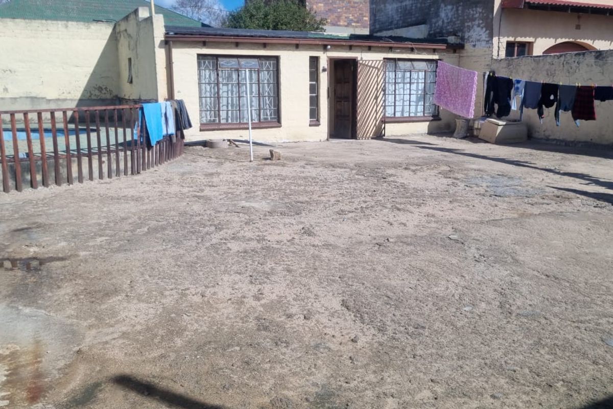 Rear exterior view of the property featuring a large concrete yard, perimeter boundary walls, and access to the main dwelling structure.