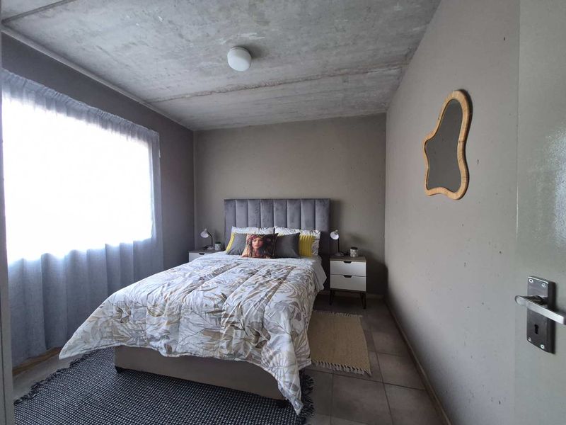 A bedroom featuring an exposed concrete ceiling, tiled flooring, and neutral wall finishes, providing a modern industrial aesthetic.