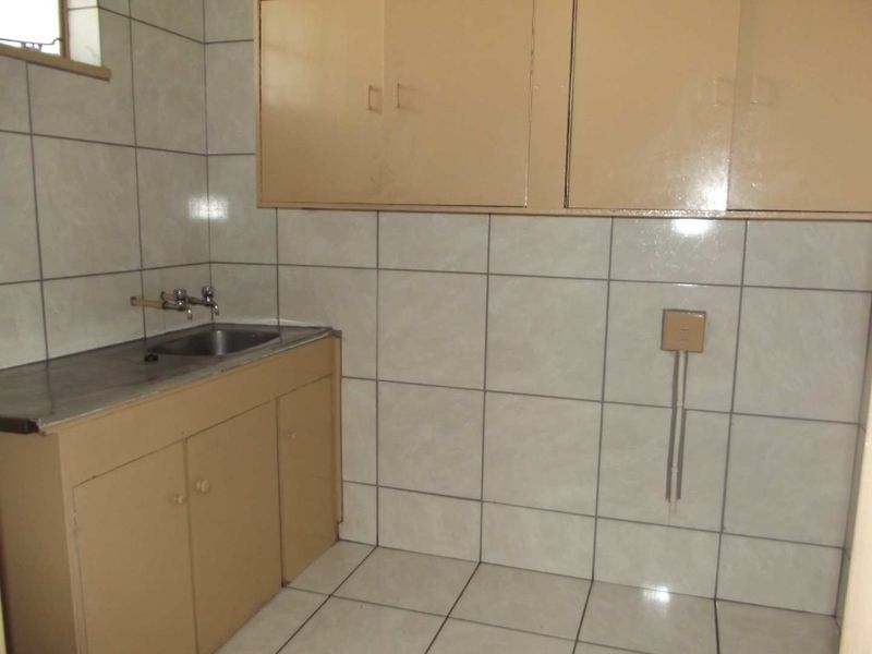 A functional laundry area featuring tiled walls, built-in cabinetry, and a stainless steel sink, offering a practical space for utility needs.
