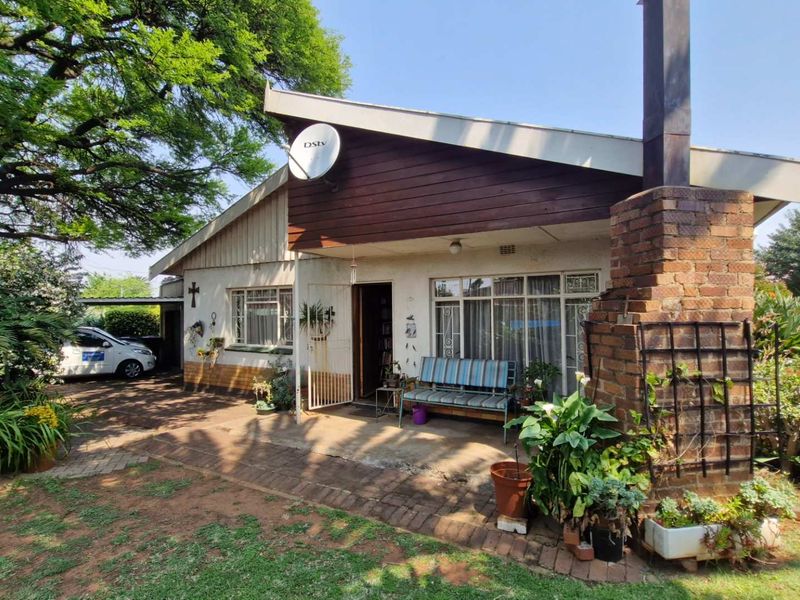 Rear exterior view of the house featuring a brick chimney, paved patio area, and timber-clad roofline set within a mature garden.