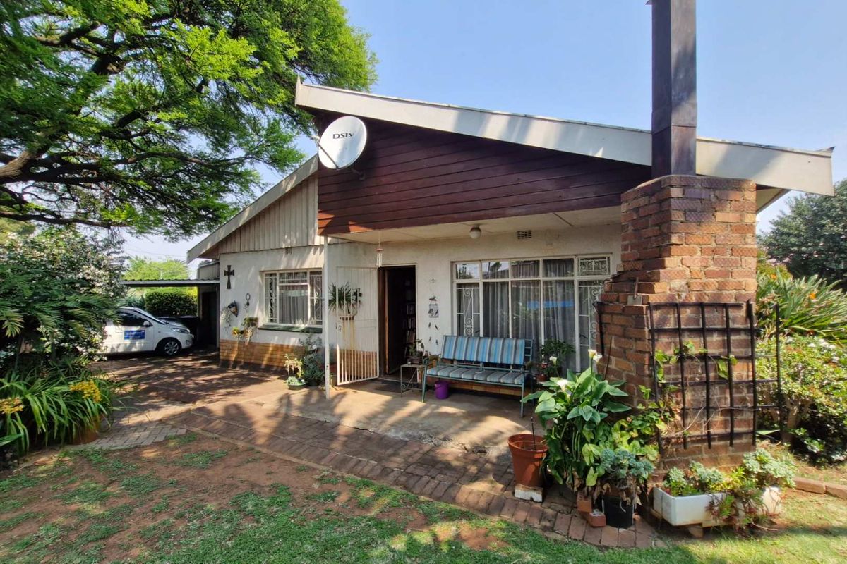 Rear exterior view of the house featuring a brick chimney, paved patio area, and timber-clad roofline set within a mature garden.