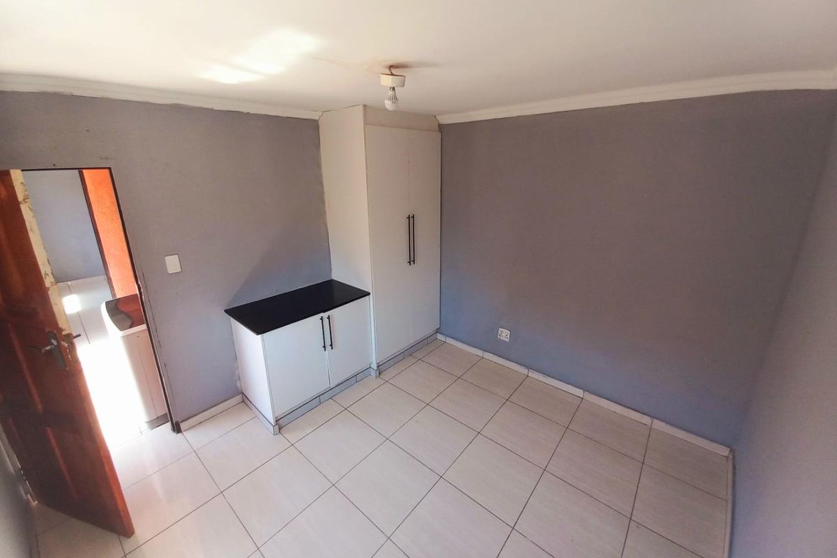 A simple bedroom featuring tiled flooring, built-in cabinetry, and a neutral grey wall finish.