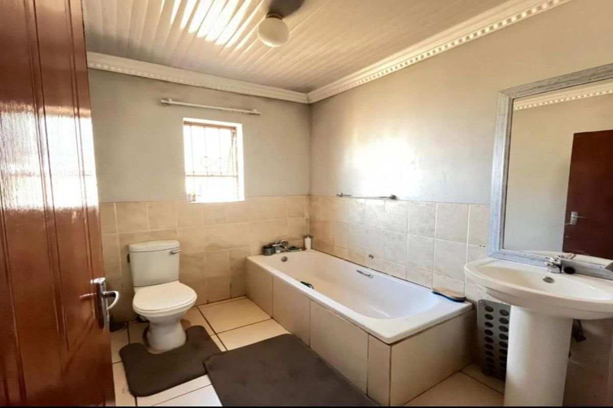 A functional bathroom featuring a bathtub, pedestal basin, and toilet with tiled walls and a wood-paneled ceiling.