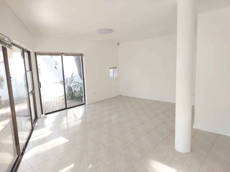 A bright, open-plan living area featuring neutral tiled flooring, a structural column, and large sliding glass doors providing access to the outdoor space.