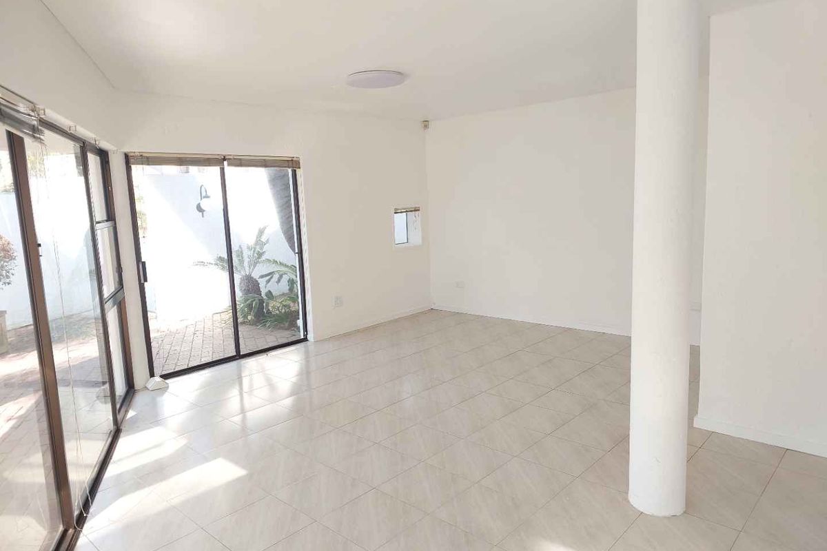 A bright, open-plan living area featuring neutral tiled flooring, a structural column, and large sliding glass doors providing access to the outdoor space.