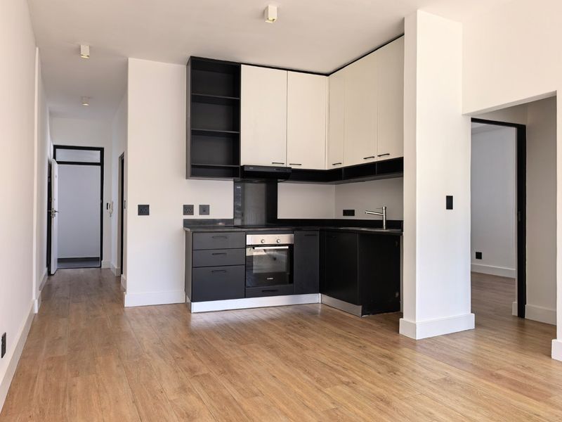 Modern, compact kitchen featuring sleek black and white cabinetry, integrated oven, extractor fan, and durable laminate flooring in an open-plan layout.