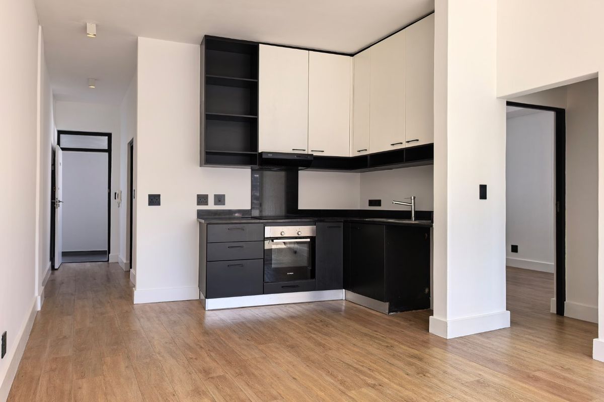 Modern, compact kitchen featuring sleek black and white cabinetry, integrated oven, extractor fan, and durable laminate flooring in an open-plan layout.