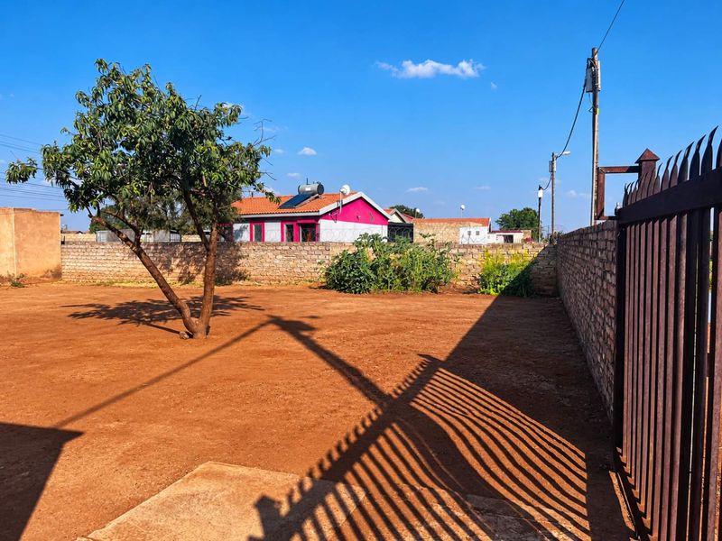 A spacious, open backyard area featuring a perimeter brick wall, metal security gate, and a clear view of the neighboring property.
