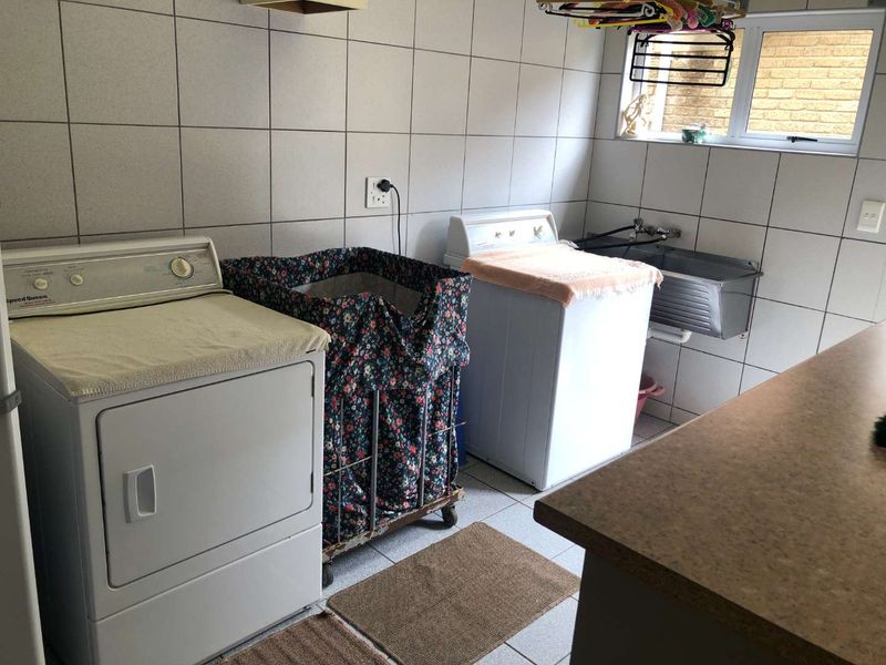 A functional laundry room featuring full-height wall tiling, a stainless steel utility sink, and dedicated space for laundry appliances.