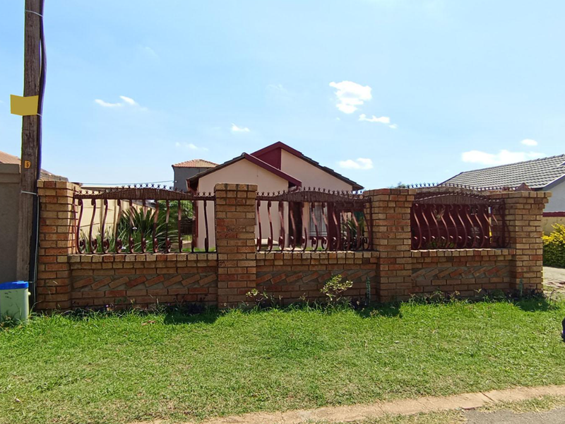 A street-facing view of the property featuring a sturdy brick boundary wall with decorative wrought iron fencing and a well-maintained front lawn.