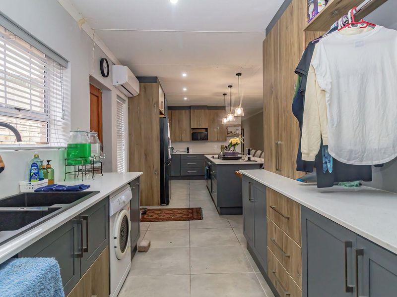 A functional scullery featuring modern two-tone cabinetry, quartz countertops, an undermount sink, and tiled flooring, providing seamless access to the main kitchen area.