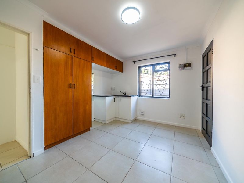 A compact kitchen area featuring tiled flooring, built-in wooden cabinetry, and a window with security bars.