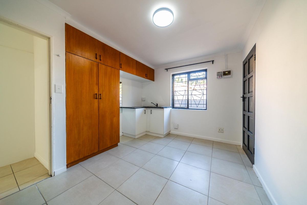 A compact kitchen area featuring tiled flooring, built-in wooden cabinetry, and a window with security bars.