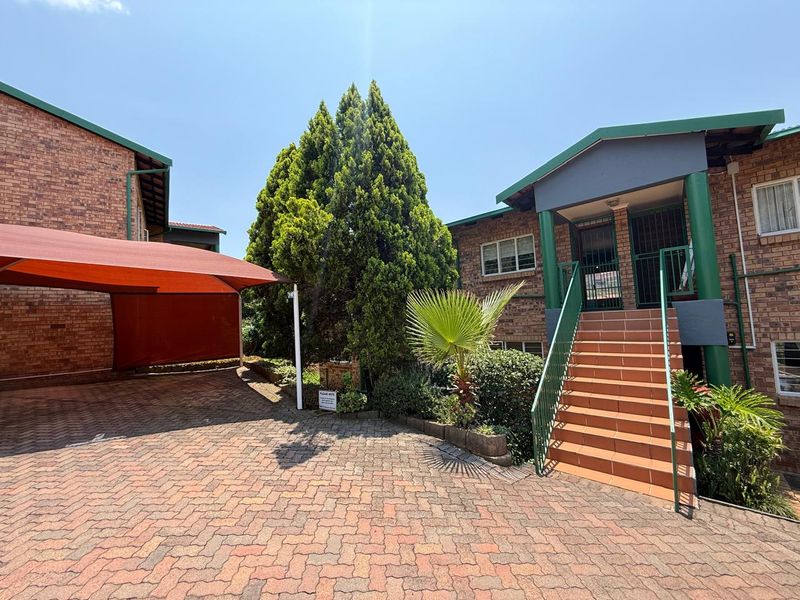 Front exterior view of the apartment complex featuring a paved driveway, covered carport, and a tiled staircase leading to the entrance.