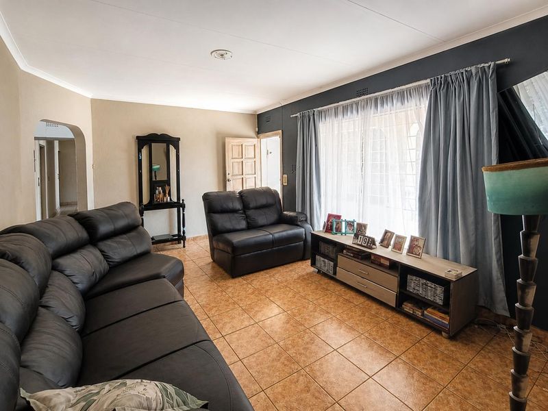 A living room featuring tiled flooring, an arched entryway, and large windows with curtain rails, providing a functional and well-lit living space.