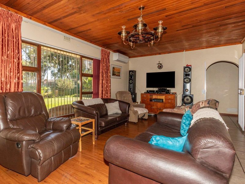 Spacious living room featuring a warm timber-paneled ceiling, laminate flooring, and large windows with security bars overlooking the garden.