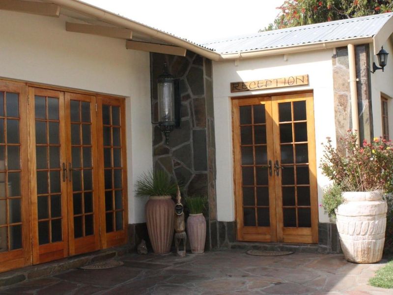The guest house entrance features a welcoming reception area with timber french doors, stone cladding accents, and a durable stone-paved patio.