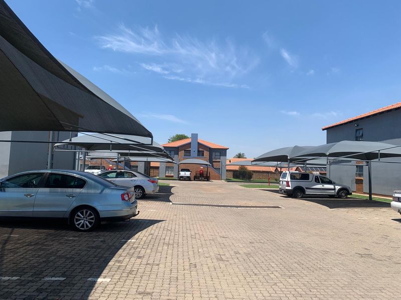Exterior view of the townhouse complex featuring a paved parking area with multiple shade cloth carports.