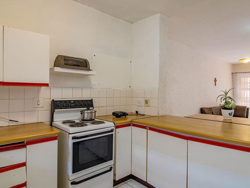 Open-plan kitchen featuring white cabinetry with red trim, laminate countertops, tiled backsplash, and a breakfast bar connecting to the living area.