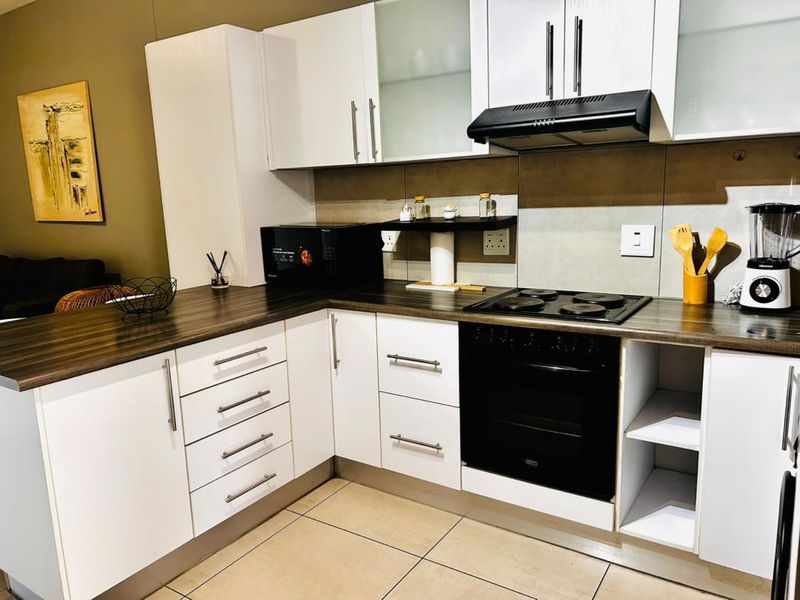 Modern kitchen featuring white cabinetry, dark laminate countertops, built-in oven, electric hob, extractor fan, and neutral tiled flooring.