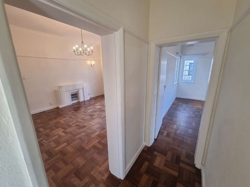 A view from the hallway looking into a living area with parquet flooring, a built-in fireplace, and classic picture rails.