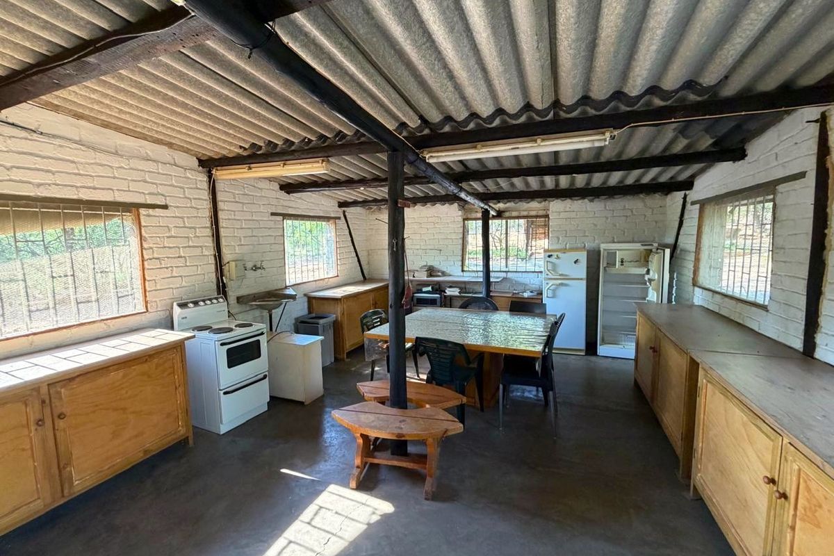 A rustic kitchen area featuring exposed timber beams, corrugated iron roofing, painted brick walls, and extensive built-in wooden cabinetry.