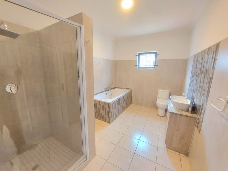 A spacious, modern bathroom featuring a glass-enclosed shower, a built-in bathtub with decorative tiling, a vanity with a vessel sink, and a toilet.