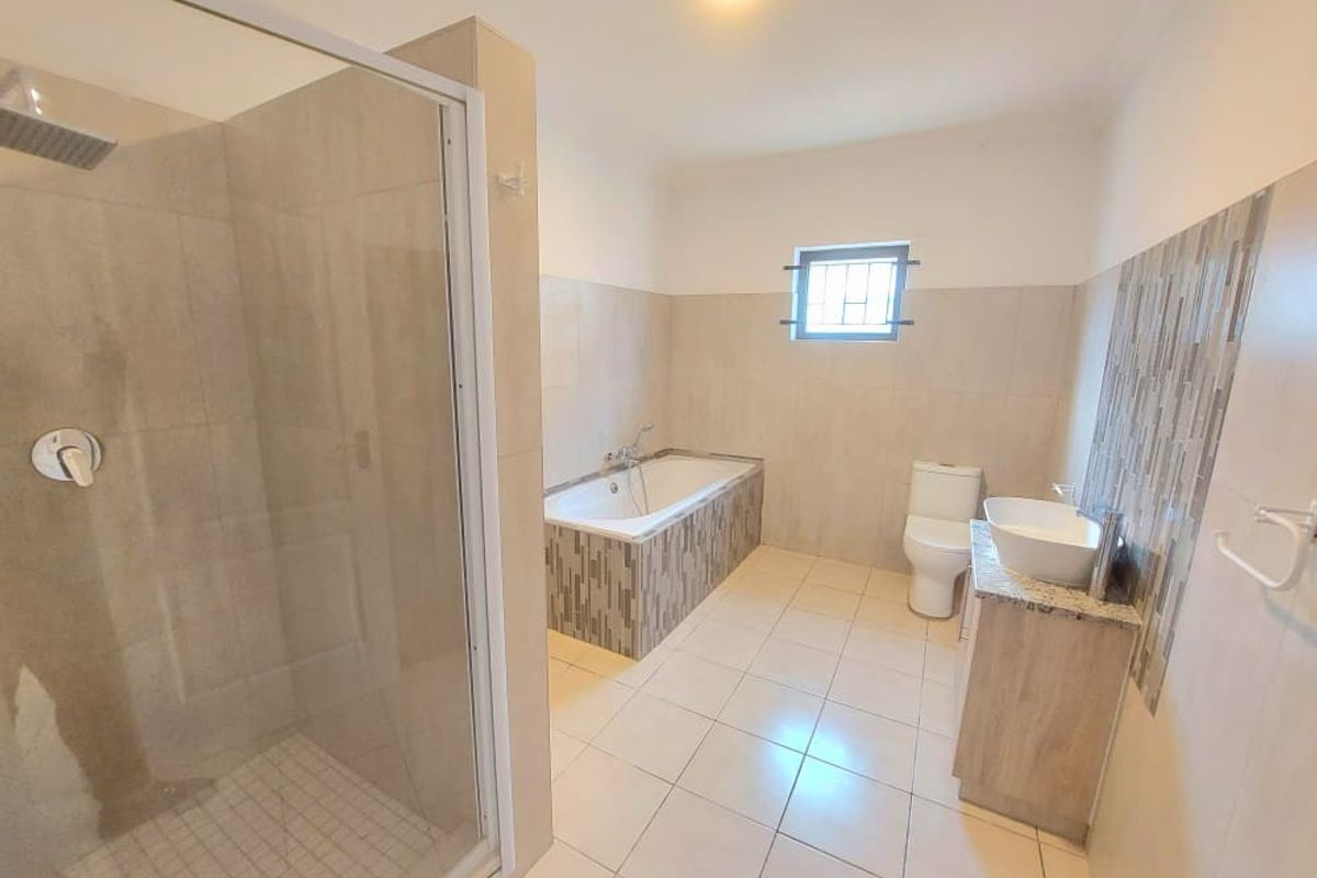 A spacious, modern bathroom featuring a glass-enclosed shower, a built-in bathtub with decorative tiling, a vanity with a vessel sink, and a toilet.