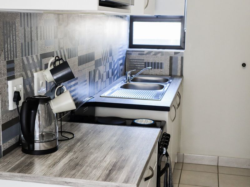 A compact kitchen featuring a double sink, laminate countertops, patterned tile backsplash, and built-in cabinetry with an integrated electric stove.