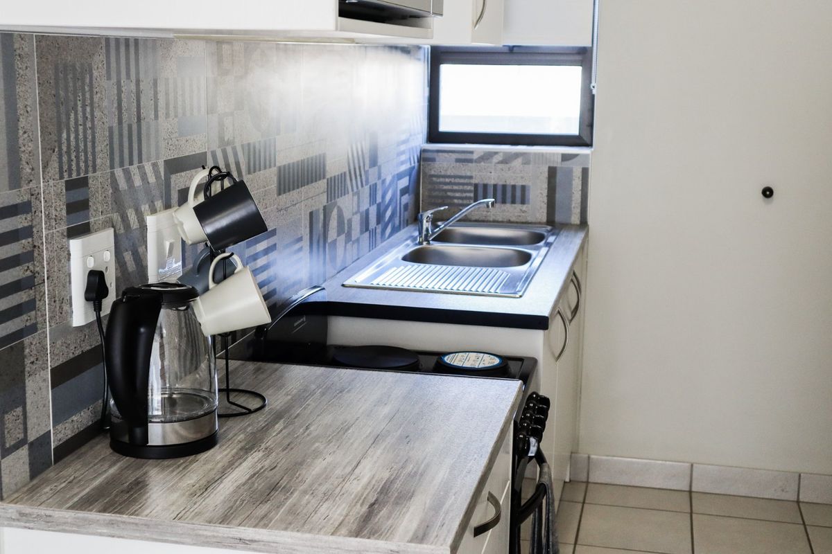 A compact kitchen featuring a double sink, laminate countertops, patterned tile backsplash, and built-in cabinetry with an integrated electric stove.