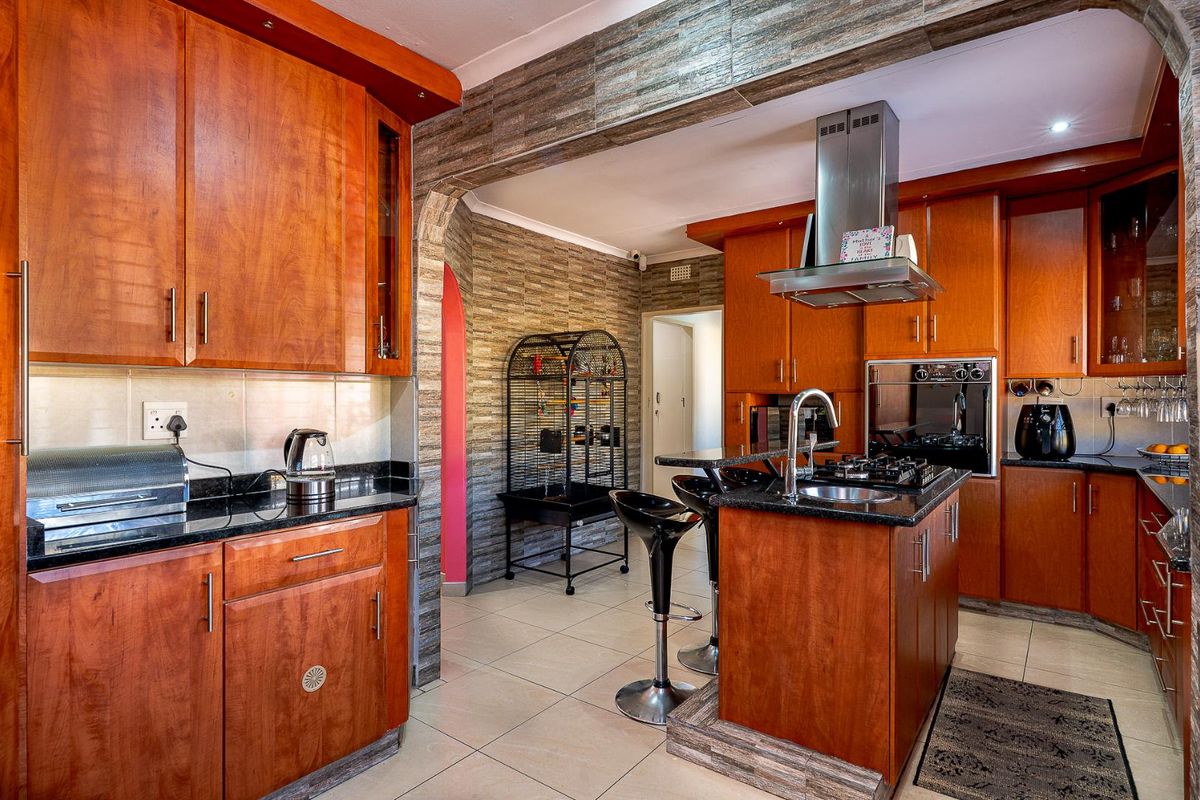 A functional kitchen featuring warm-toned wooden cabinetry, granite countertops, a central island with a sink, and a stainless steel extractor fan.
