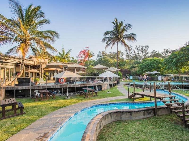 Expansive outdoor leisure area featuring a swimming pool, raised timber decking, and a pedestrian bridge set within a landscaped garden environment.