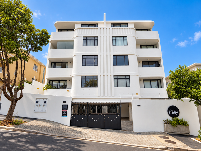 A well-maintained modern apartment building facade featuring clean white lines, secure gated access, and private balconies.