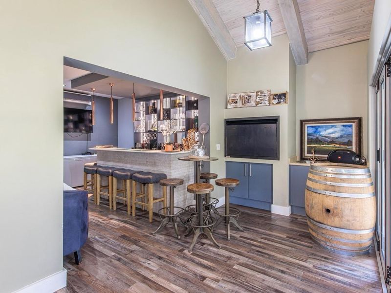 A well-appointed indoor bar area featuring a built-in counter, cabinetry, fireplace, and exposed timber ceiling beams, creating a sophisticated space for entertaining.