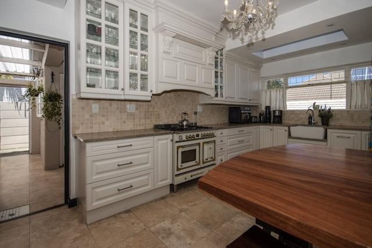 A well-appointed kitchen featuring classic white cabinetry, stone countertops, a farmhouse sink, a gas range, and a skylight, with an adjacent utility area.