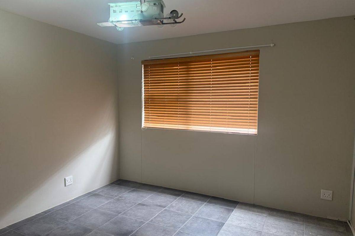 A clean, empty bedroom featuring neutral wall tones, dark tiled flooring, and fitted wooden venetian blinds.